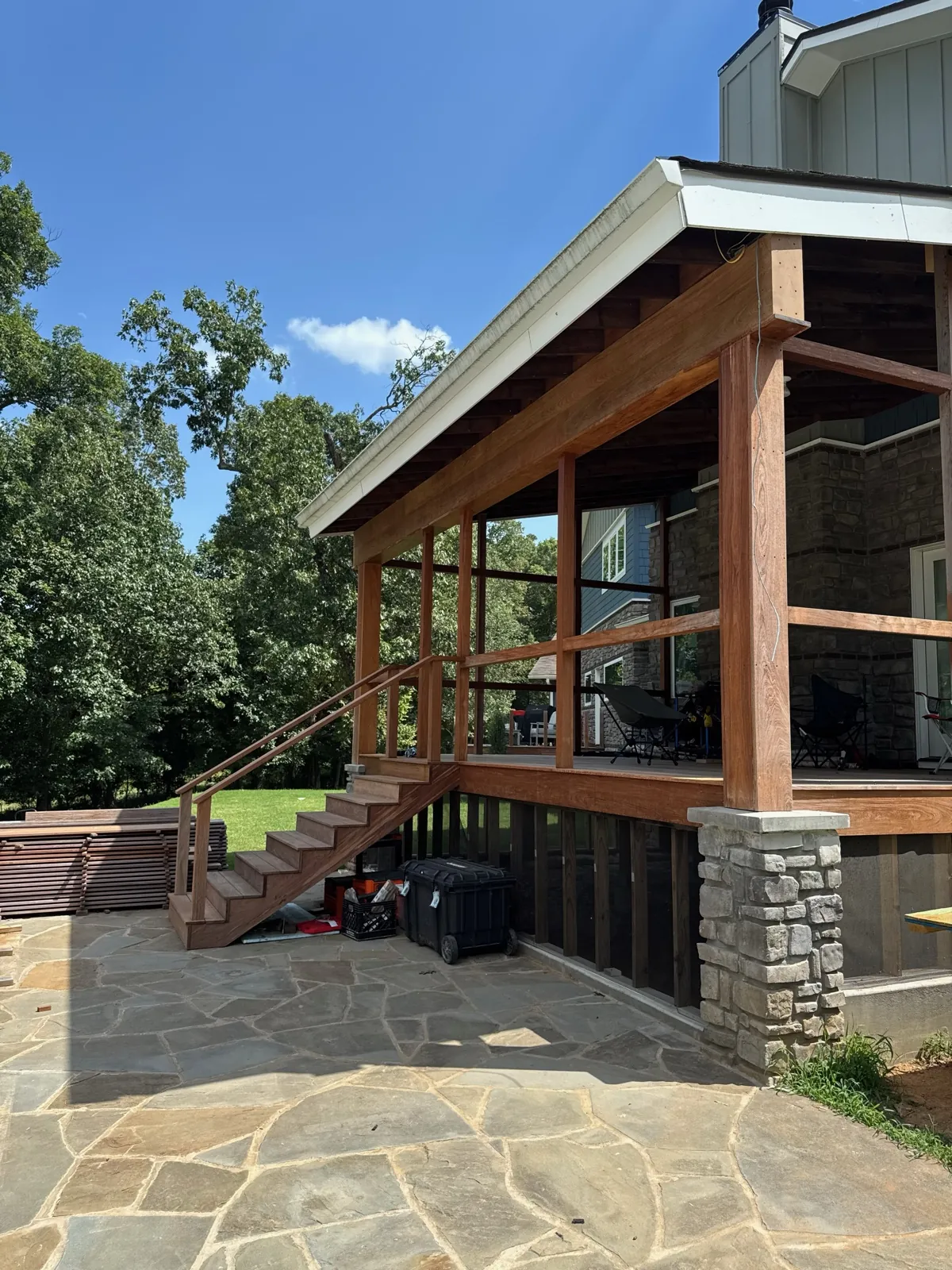 Covered porch with stone base, staircase, and patio